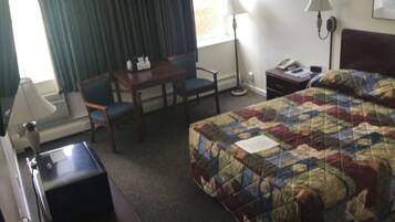 A hotel room with a bed, a desk, a chair, a lamp, and a telephone.