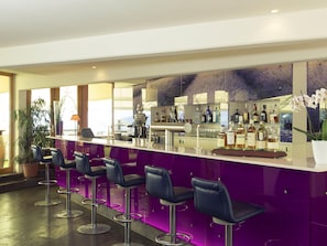 A bar area with a purple counter, multiple stools, and a variety of bottles.