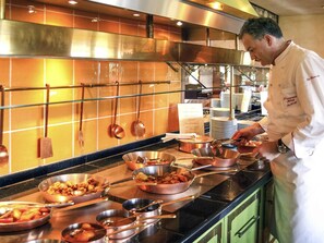 A chef preparing food in a kitchen with stainless steel appliances and a tiled backsplash. - Mercure Hotel Panorama Freiburg (Freiburg im Breisgau)