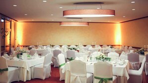 Une salle de banquet avec des tables rondes, des nappes blanches et des chaises ornées de rubans verts.