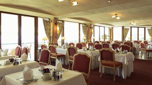 Un espace repas avec des tables dressées, de grandes fenêtres et un ventilateur de plafond.