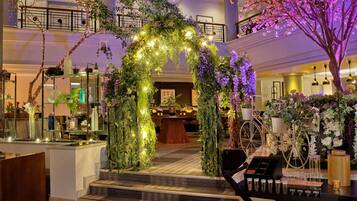 Un vestíbulo con un arco central adornado con plantas y luces de cuerda, rodeado de macetas y una bicicleta antigua.