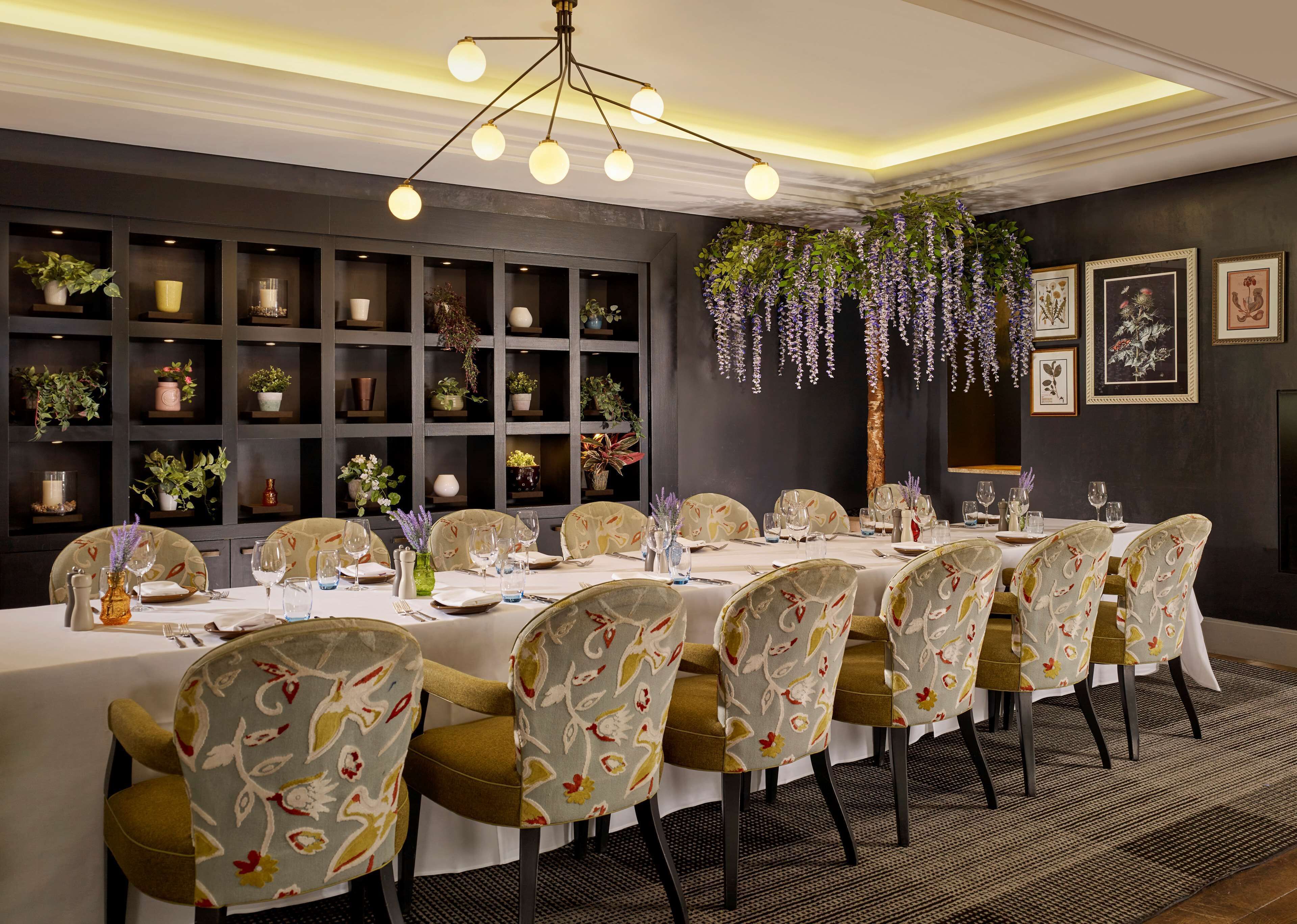 A dining room with a long table set for a meal, surrounded by chairs with floral upholstery.