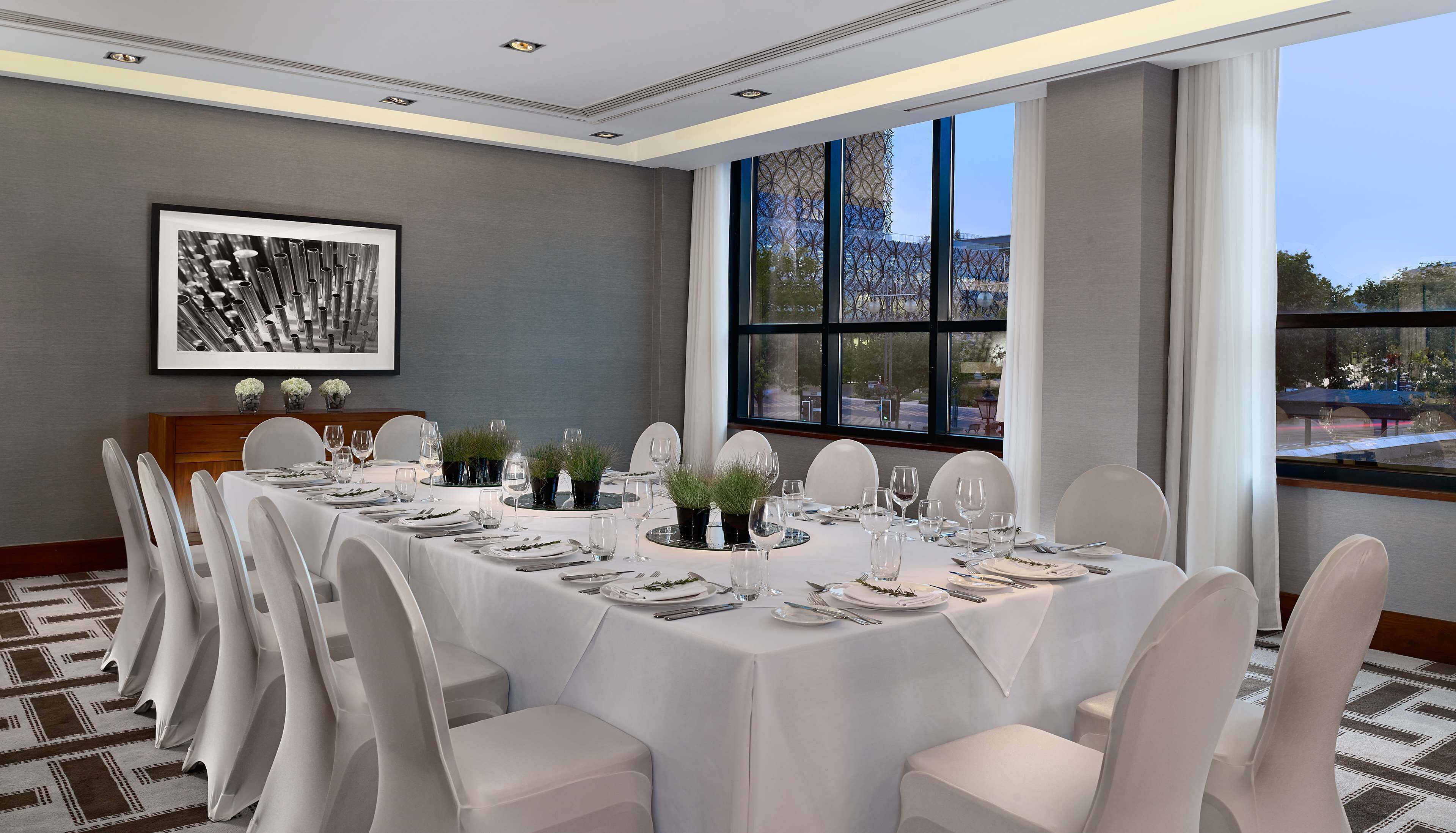 A conference room with a long table set for a meeting, large windows, and a framed artwork on the wall.
