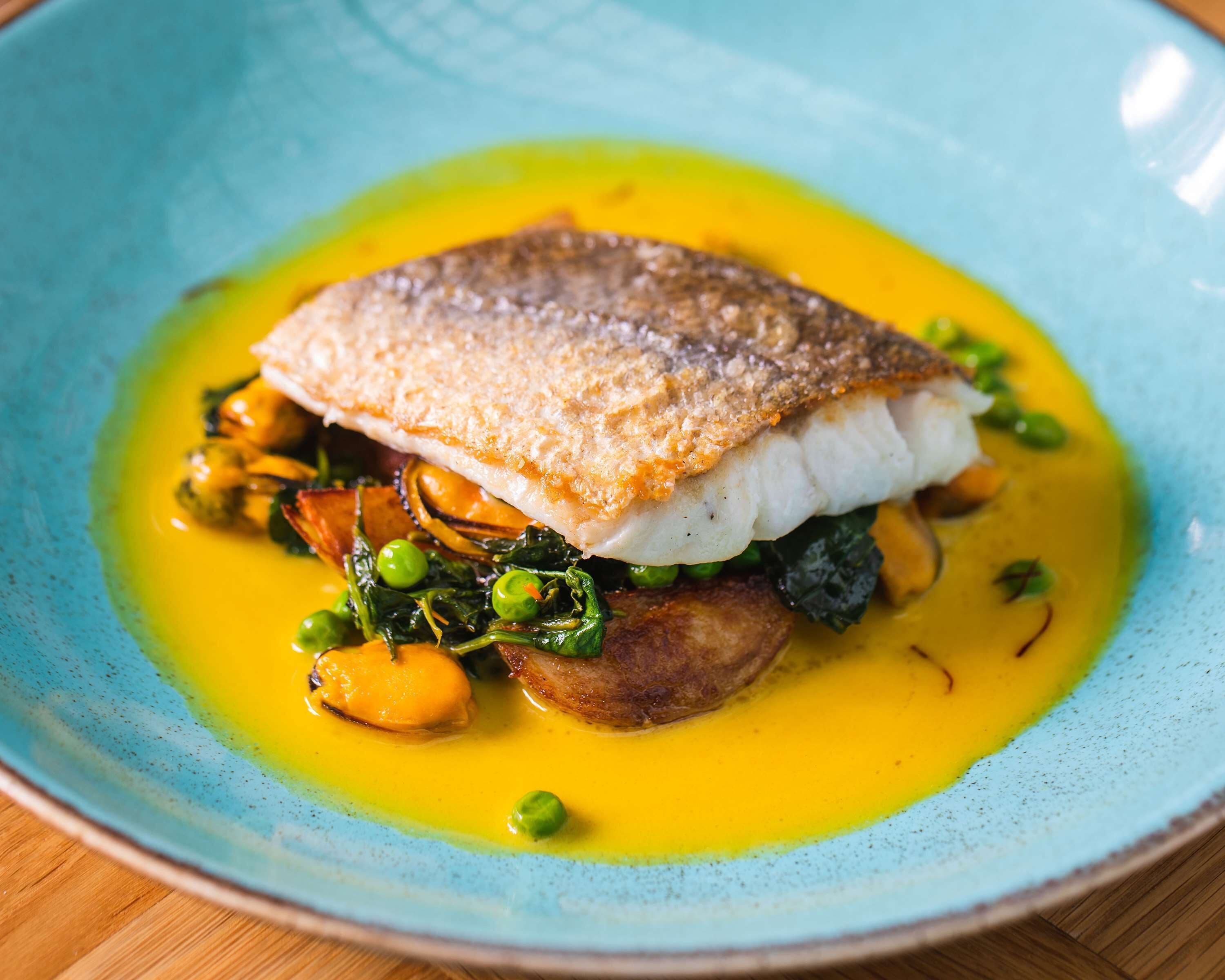 A plate of food with a piece of fish, vegetables, and a yellow sauce.
