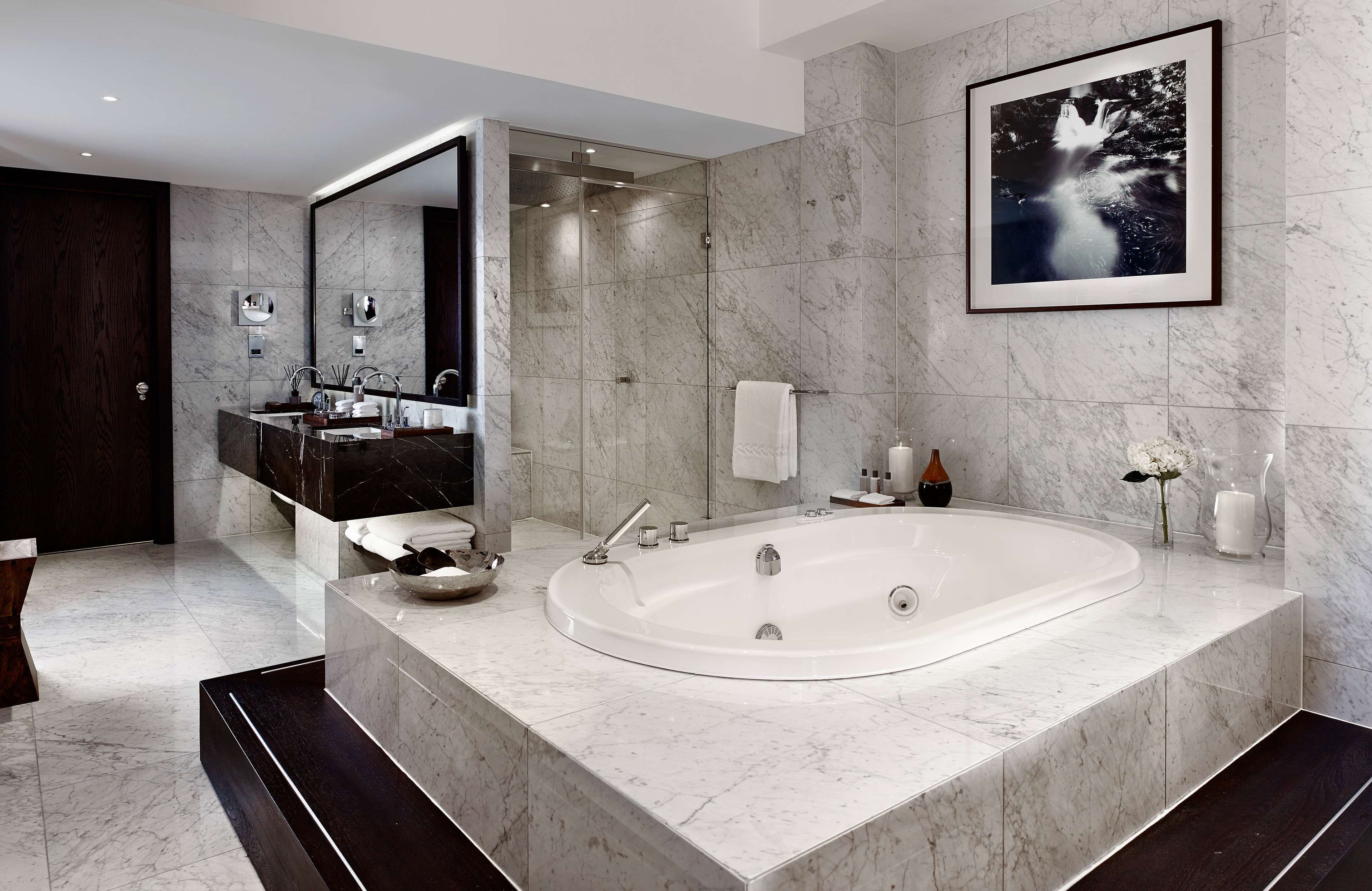 A modern bathroom with a large bathtub, a double vanity with a mirror, and a framed artwork on the wall.
