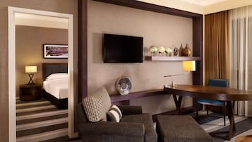 A hotel room with a bed, a TV mounted on the wall, a dining table, and a seating area with a sofa and chairs.