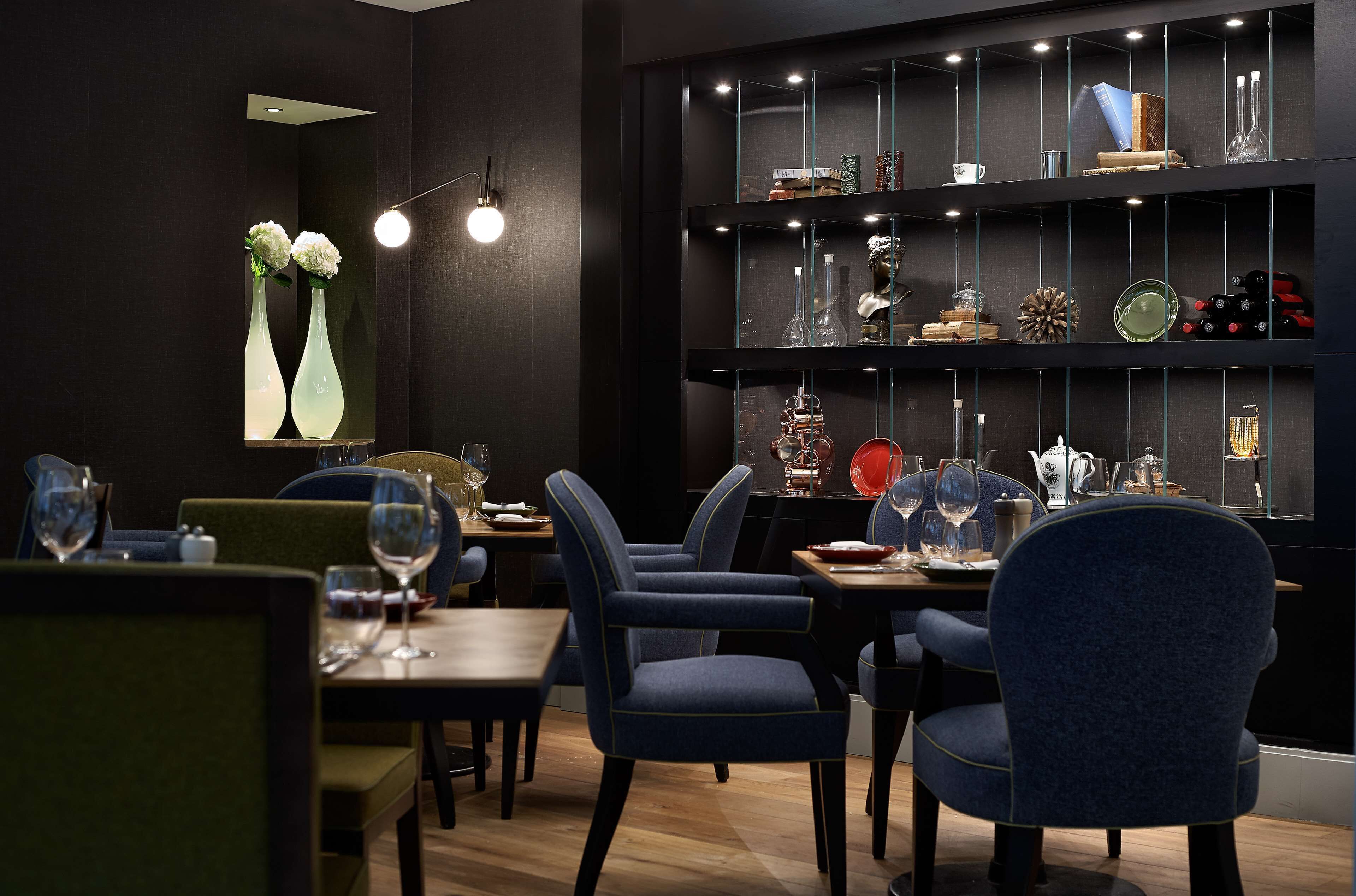 A restaurant interior with dark walls, blue upholstered chairs, and a glass display case with various items.