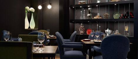 Interior de restaurante con paredes oscuras, sillas tapizadas en azul y una vitrina de cristal con diversos objetos.