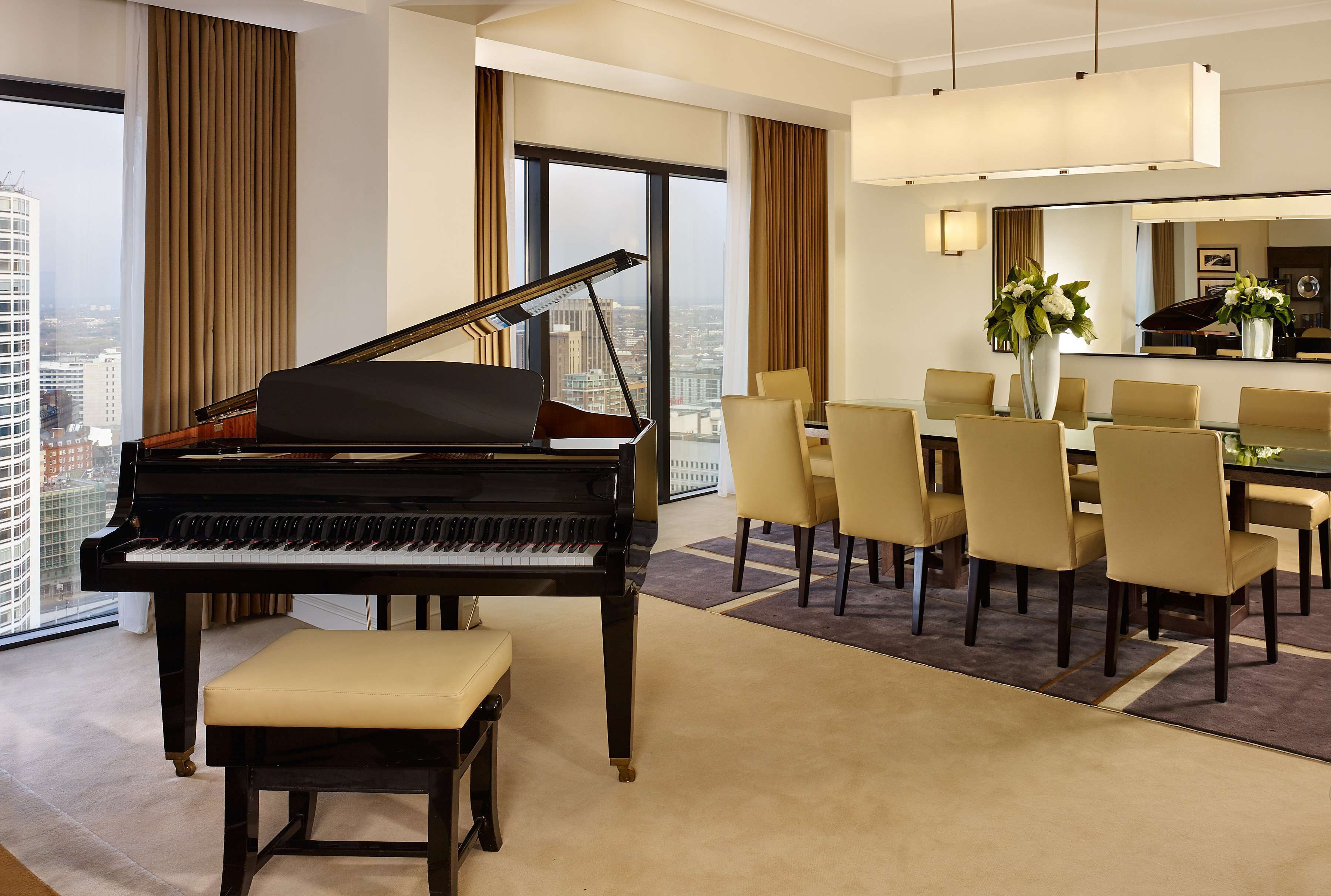Un magnifique piano à queue se trouve dans une pièce spacieuse, qui comprend un coin repas et une grande fenêtre donnant sur la ville.
