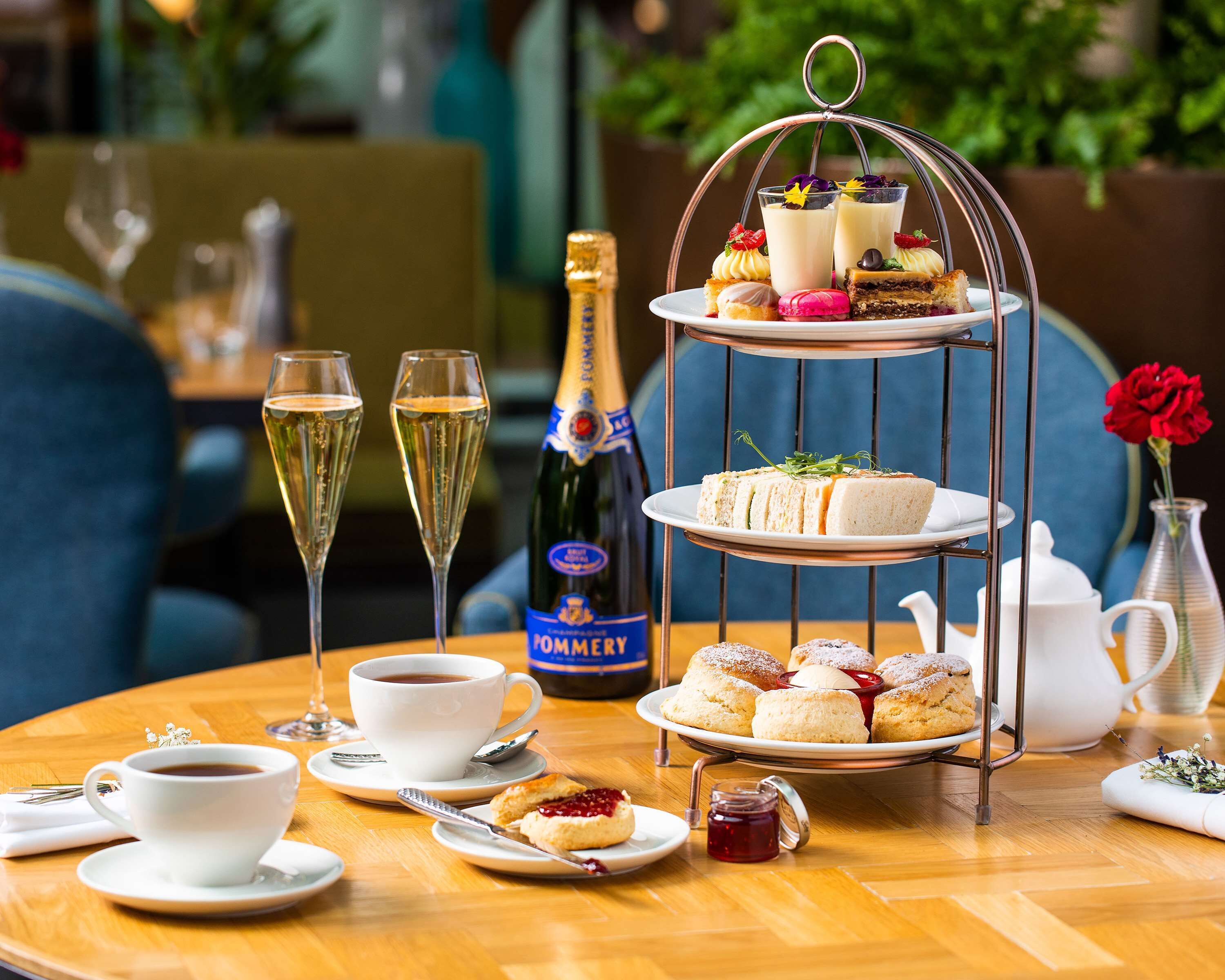 A table set with a tiered dessert stand, a bottle of champagne, and a cup of coffee.