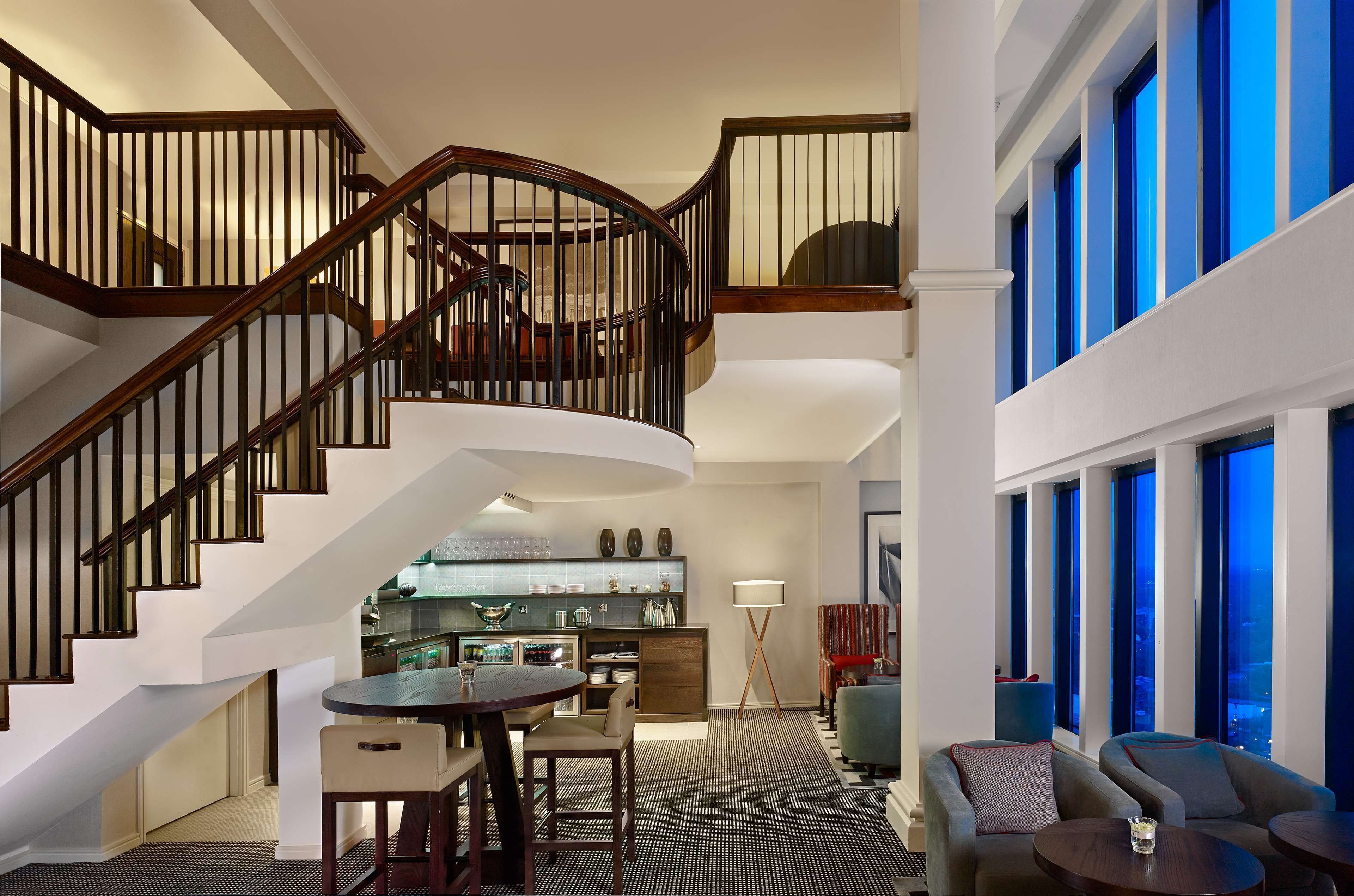 A spacious interior with a curved staircase, a dining area, and a seating area with large windows.