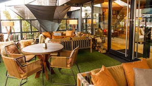 An indoor seating area with round tables and wicker chairs, a sofa with orange cushions, and a large window offering a view of the interior. - Hyatt Regency Birmingham (Birmingham)