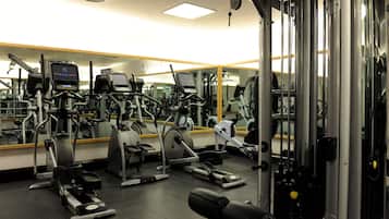 Un gimnasio con diferentes máquinas de ejercicio, un espejo grande en la pared y una lámpara en el techo.