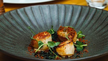 A plate of seared scallops with greens and a textured crust, set on a dark plate.