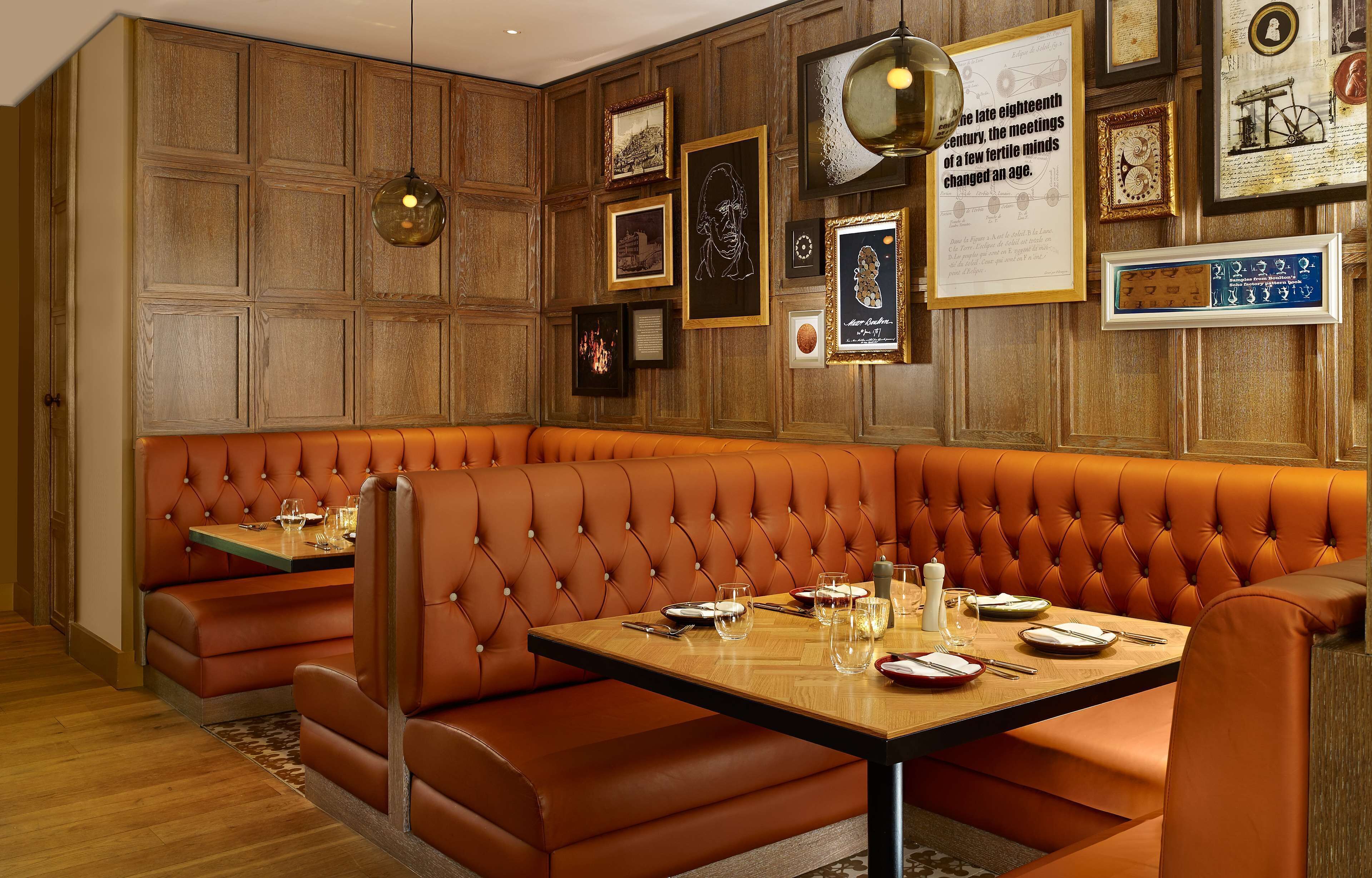A restaurant with a long brown leather booth seating area and a wooden wall adorned with framed pictures and a clock.