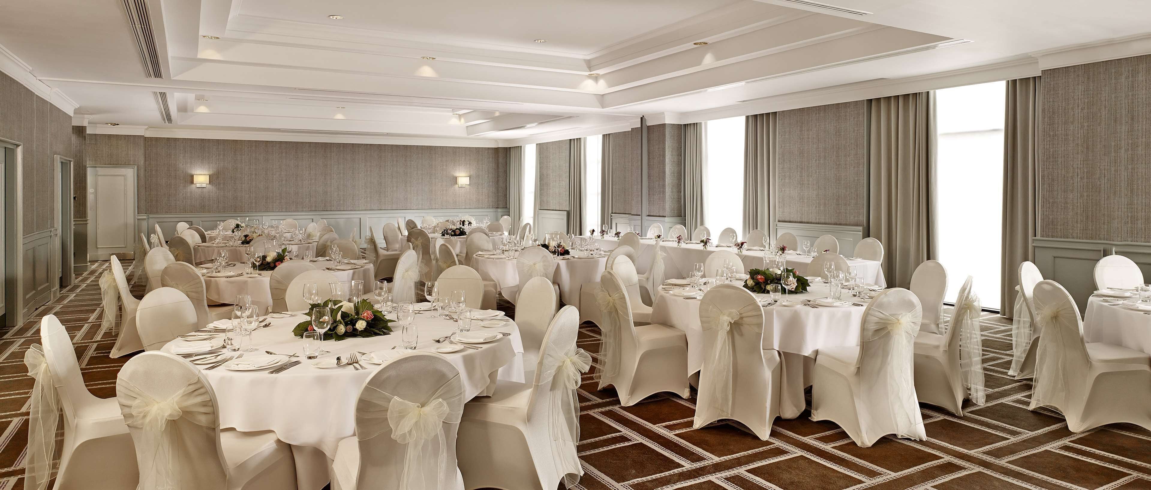 Une salle de banquet dotée de nombreuses tables rondes, chacune recouverte d’une nappe blanche et agrémentée de chaises et de décorations de table.