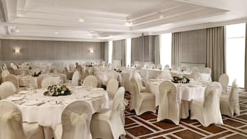 Une salle de banquet dotée de nombreuses tables rondes, chacune recouverte d’une nappe blanche et agrémentée de chaises et de décorations de table.