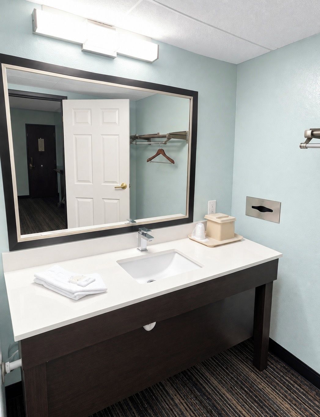 Un baño de hotel con un lavamanos blanco, tocador de madera oscura, un espejo grande y un perchero para toallas.