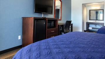 A hotel room with a large bed, a television, a desk with a chair, and a mirror.