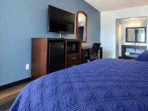 A hotel room with a large bed, a television, a desk with a chair, and a mirror. - Executive Inn (Muskogee)