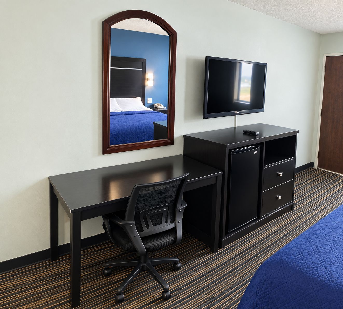 A hotel room with a bed, a desk with a chair, a television, and a wardrobe.