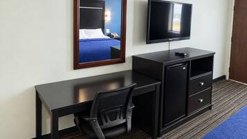 A hotel room with a bed, a desk with a chair, a television, and a wardrobe.