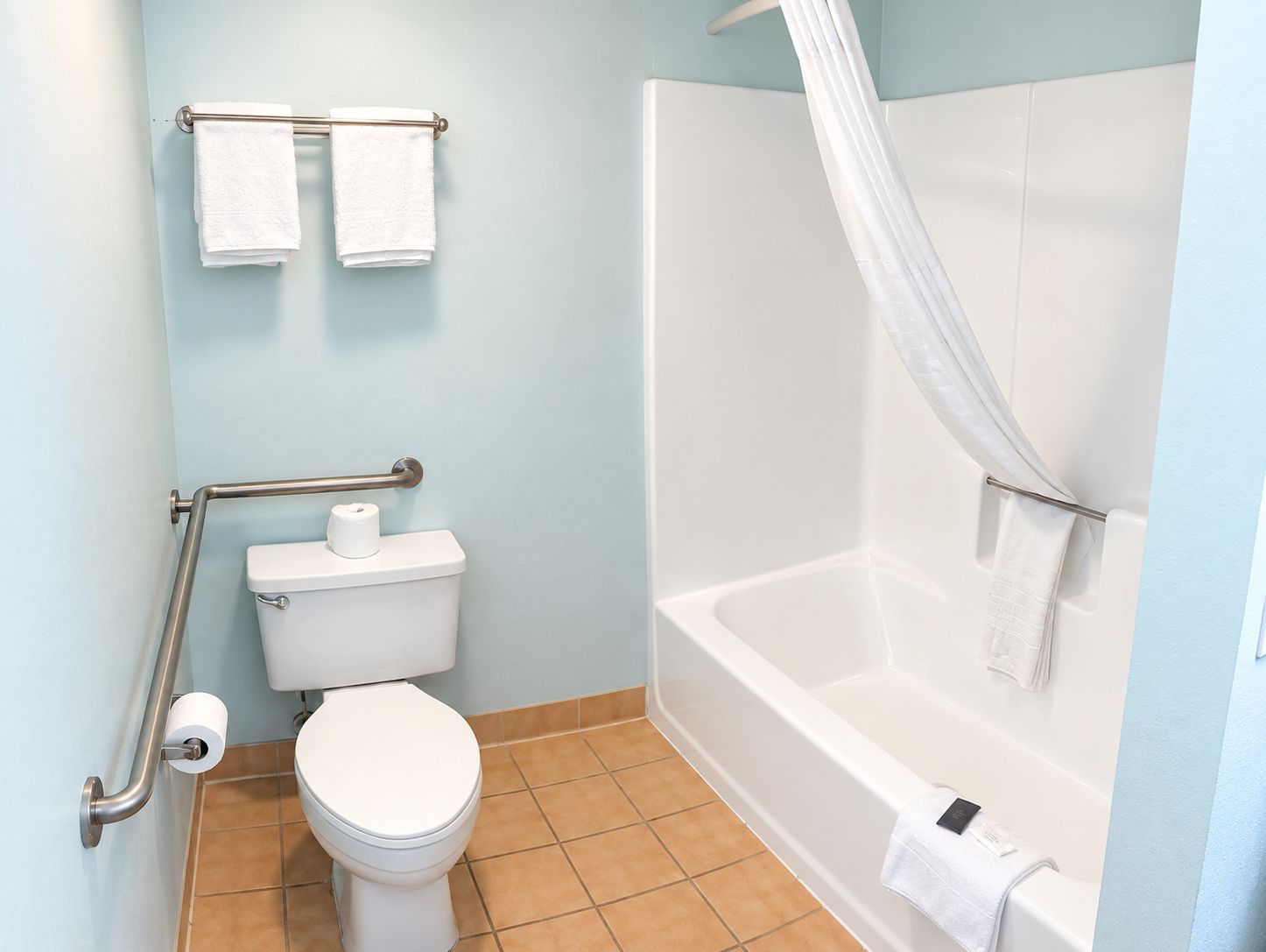 A bathroom with a toilet, a shower with a curtain, and two towels on a rack.