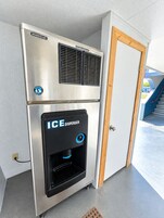 Un dispensador de hielo compacto con acabado metálico, situado en una esquina junto a una puerta blanca.