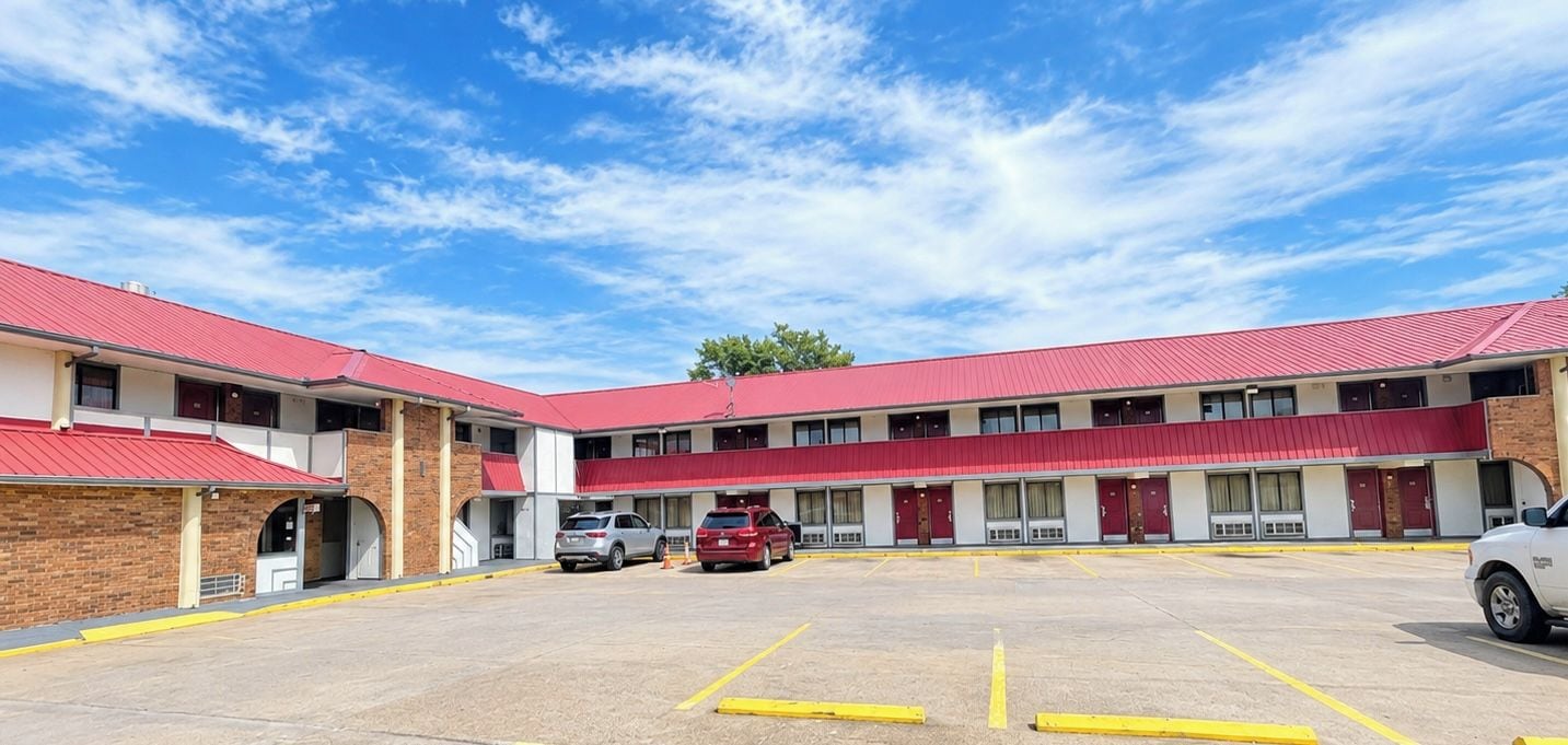 A motel with a red roof, multiple rooms, and a parking lot.