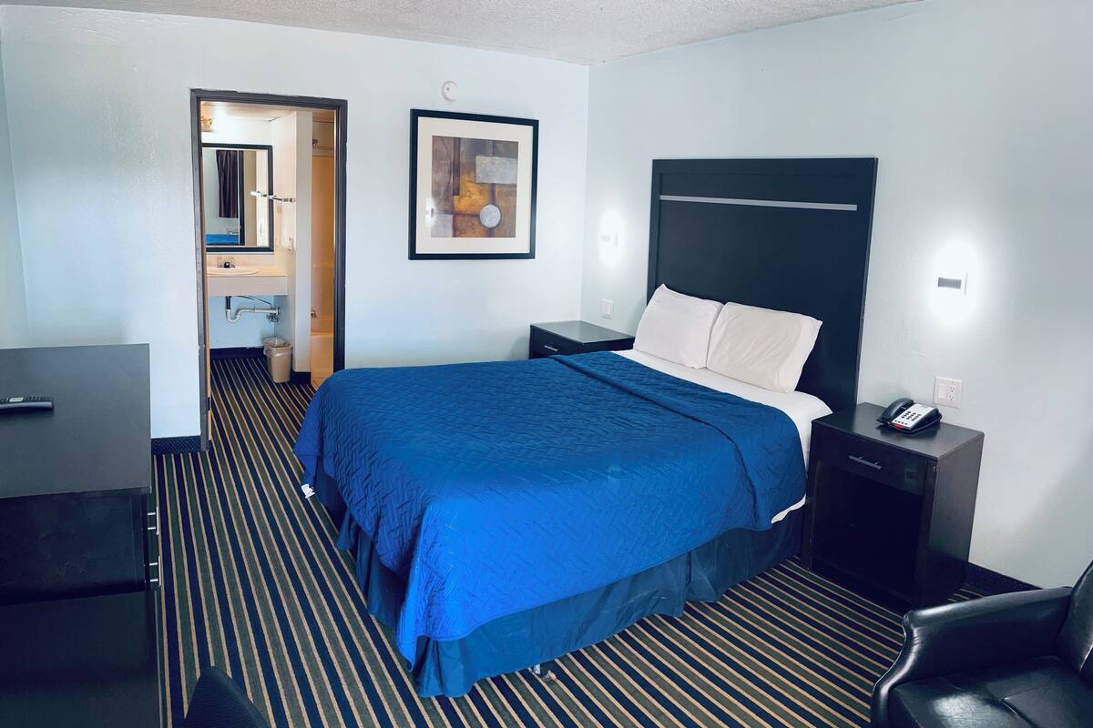 A hotel room with a bed, bedside table, chair, and a bathroom visible through an open door.