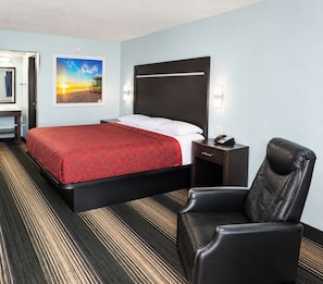 A hotel room with a bed, a desk, a chair, and a painting on the wall.