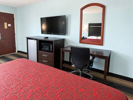 Habitación de hotel con cama, escritorio, silla, televisión, microondas y espejo.