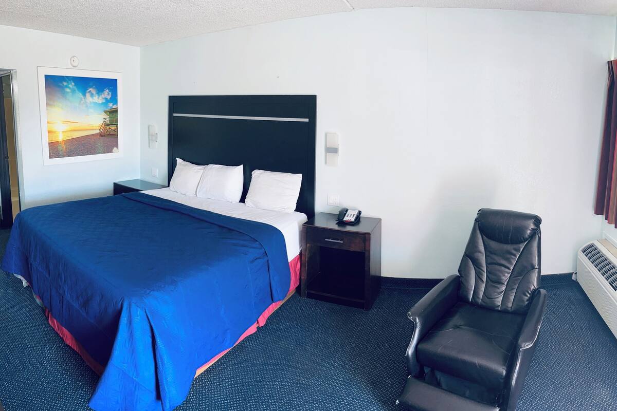 A hotel room with a large bed, a chair, a nightstand, a telephone, and a picture on the wall.