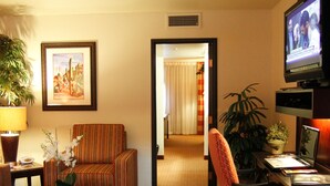Een hotelkamer met een gestreepte fauteuil, een bureau met een computer, een televisie en een potplant.