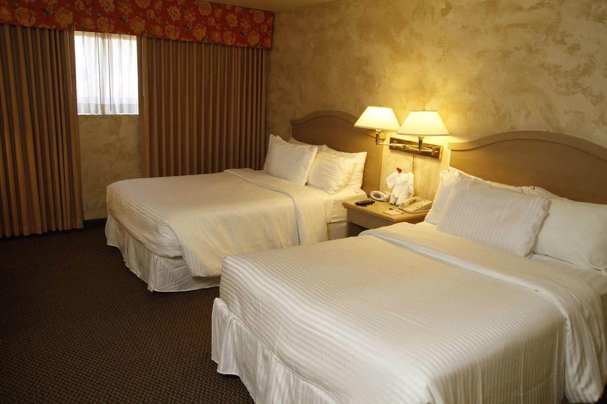 A hotel room with two beds, a nightstand with a lamp, and a telephone.