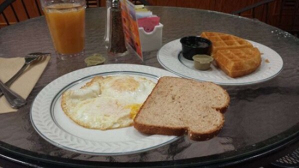 Un plato de desayuno con huevos, tostadas y un gofre sobre una mesa de vidrio.