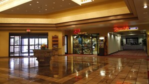 Een ruime lobby met een gepolijste tegelvloer, een grote sierplanter en een winkel met 'Fine Gifts'.