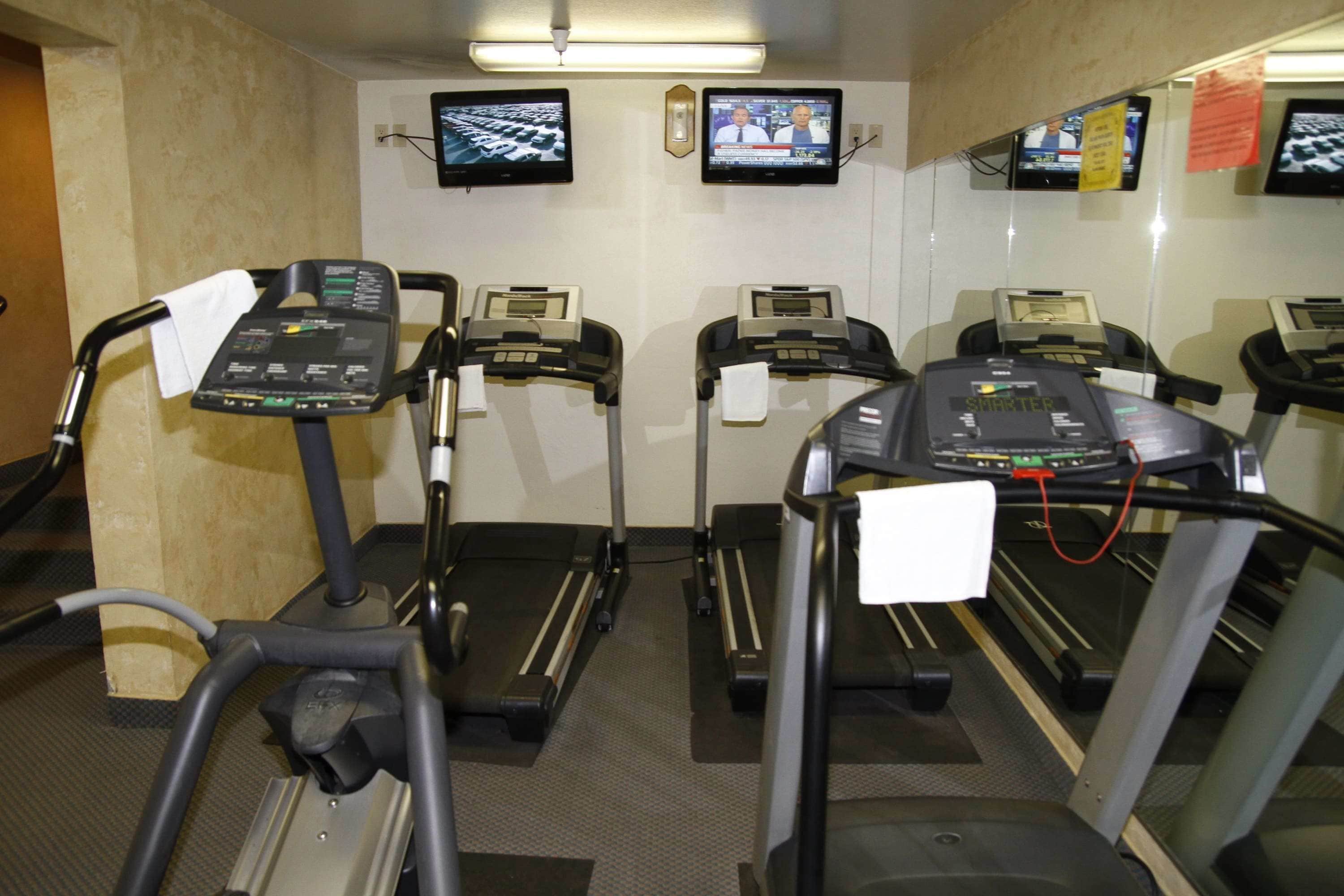 Gimnasio con cintas de correr, cada una con panel de control y pantalla que muestra noticias.