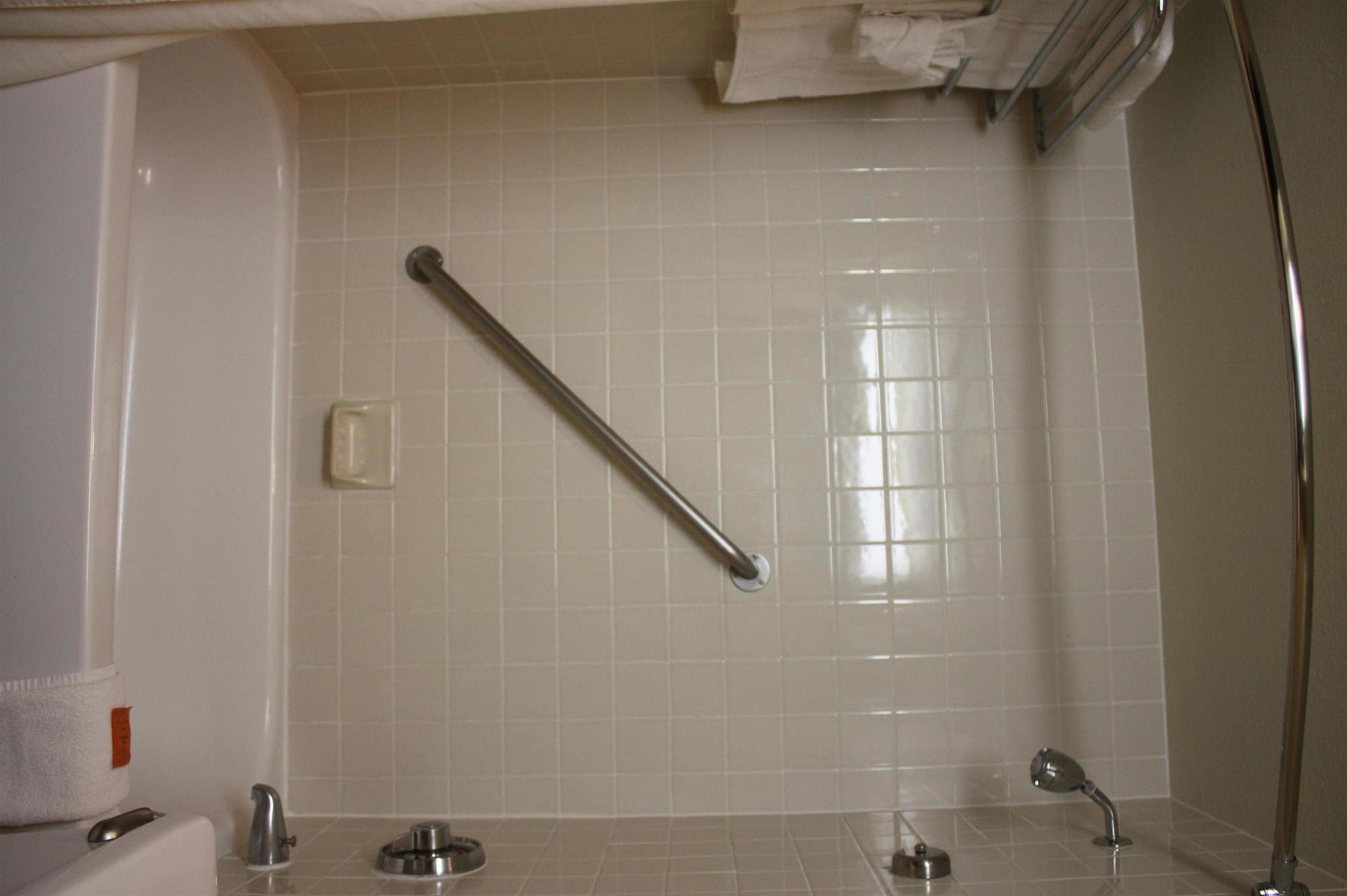 A bathroom with white tiles, a grab bar, a towel rack, and a mirror.