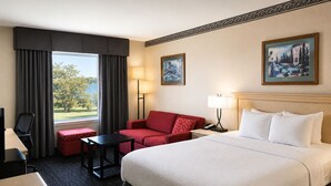 A hotel room with a large bed, a red sofa, a small table, a desk with a chair, a lamp, and two paintings on the wall. - Ramada by Wyndham Trenton (Quinte West)