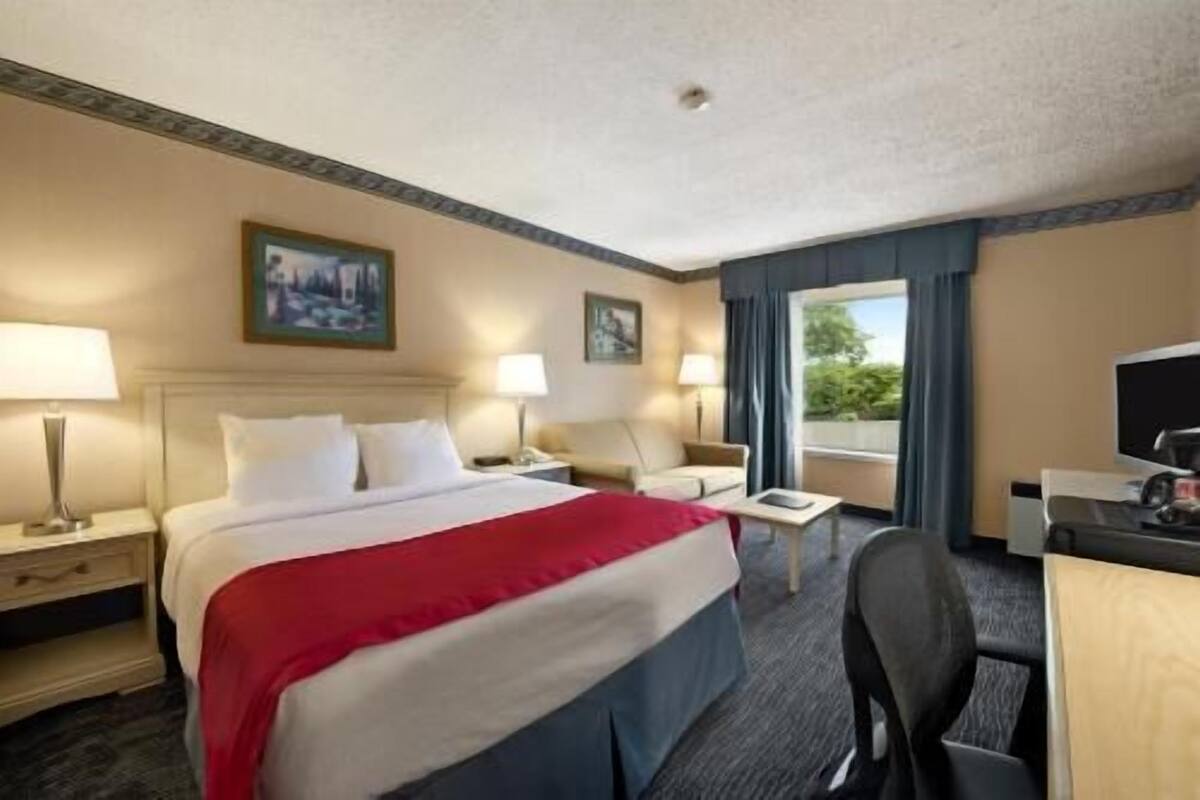 Habitación de hotel con cama, dos mesitas de noche con lámparas, escritorio con silla y ventana con cortinas.