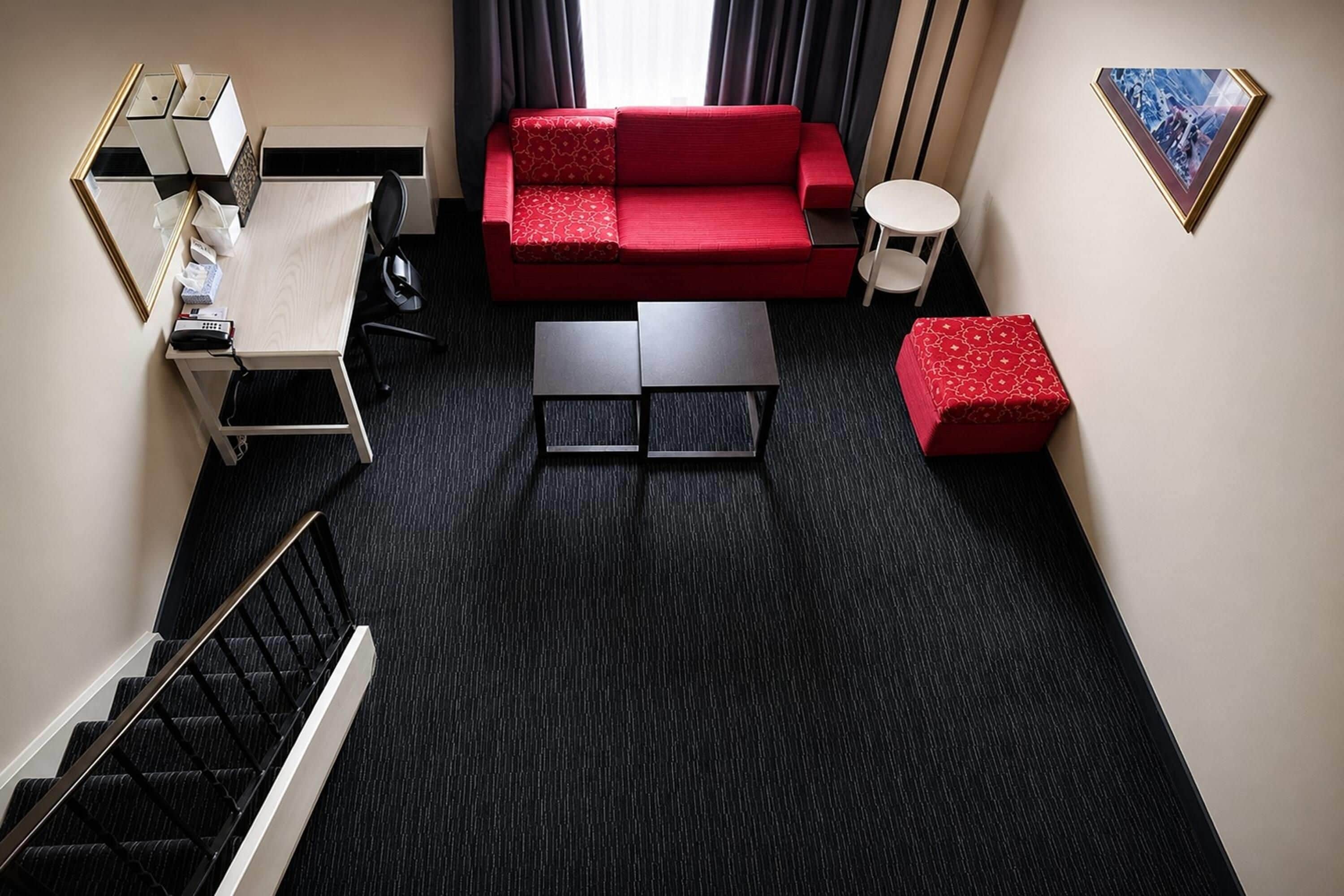 Un espacio habitable compacto con un sofá rojo, una mesita de centro, una mesita auxiliar y una escalera que sube a un nivel superior.
