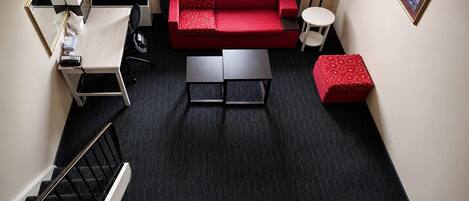 A compact living space with a red sofa, a small coffee table, a side table, and a staircase leading to an upper level.