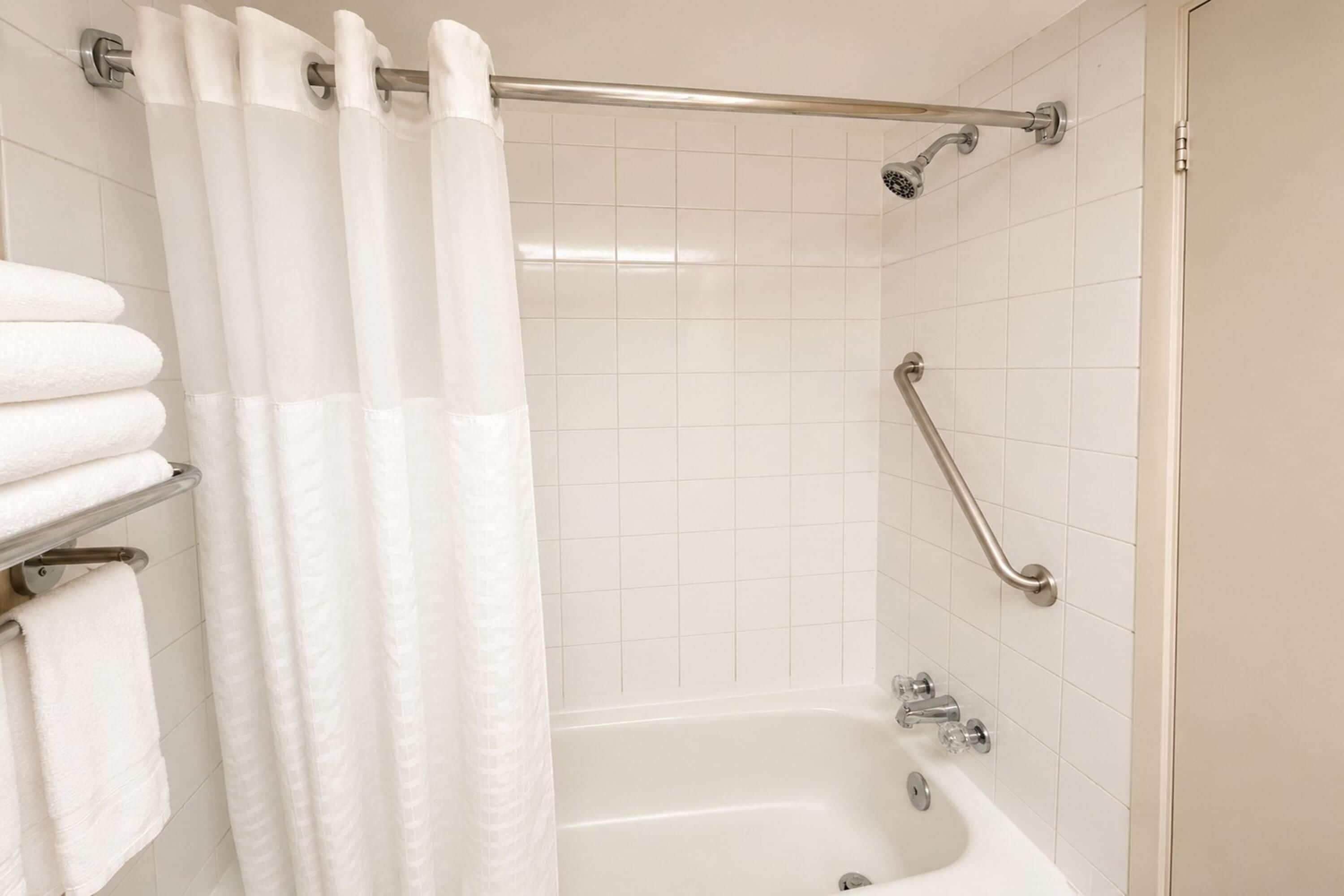 A bathroom with a bathtub, a shower, and a handrail.