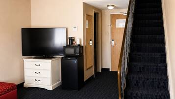 A hotel room with a TV, a mini-fridge, a desk, a chair, a staircase, and a door leading to another room.