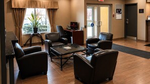 A hotel lobby with leather chairs, a reception desk, a computer, and an exit sign. - Ramada by Wyndham Trenton (Quinte West)
