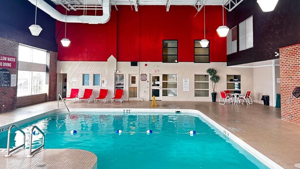 An indoor swimming pool with clear water, red chairs, and a red wall. - Ramada by Wyndham Trenton (Quinte West)