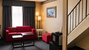 A hotel room with a red sofa, a small table, a lamp, a microwave, and a staircase. - Ramada by Wyndham Trenton (Quinte West)