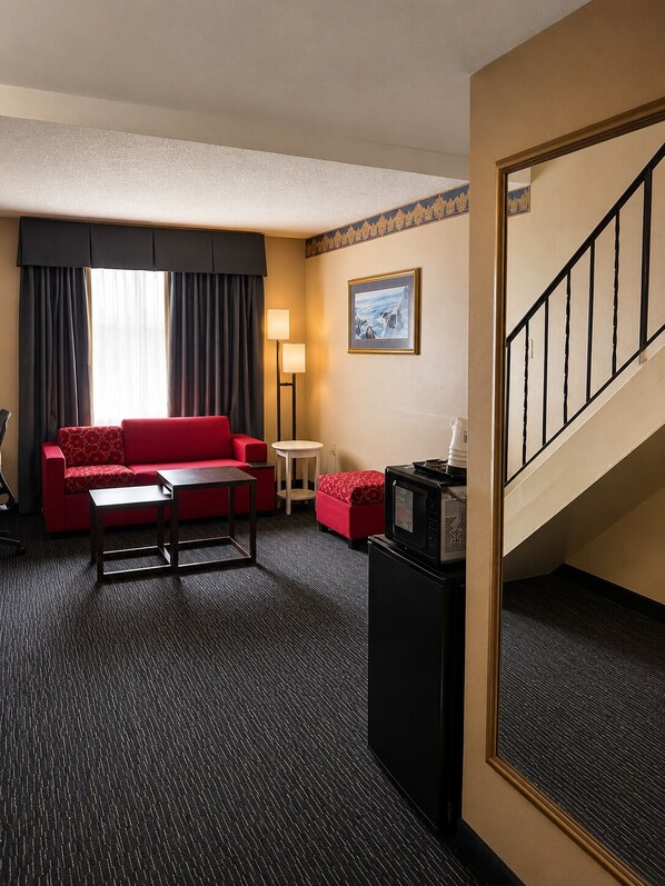 Habitación de hotel con sofá rojo, una mesita, lámpara, microondas y una escalera.